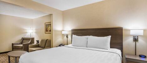 A hotel room with a large bed, two bedside lamps, a chair, a small table, and a nightstand with a clock.