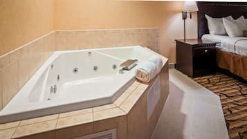 Un bagno d'albergo con una vasca da bagno ampia, un comodino e un letto con cuscini.