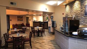 Eine Hotelhalle mit einer Sitzecke, einem Empfangstresen mit einer Kaffeemaschine und einer Wand mit einer strukturierten Oberfläche.