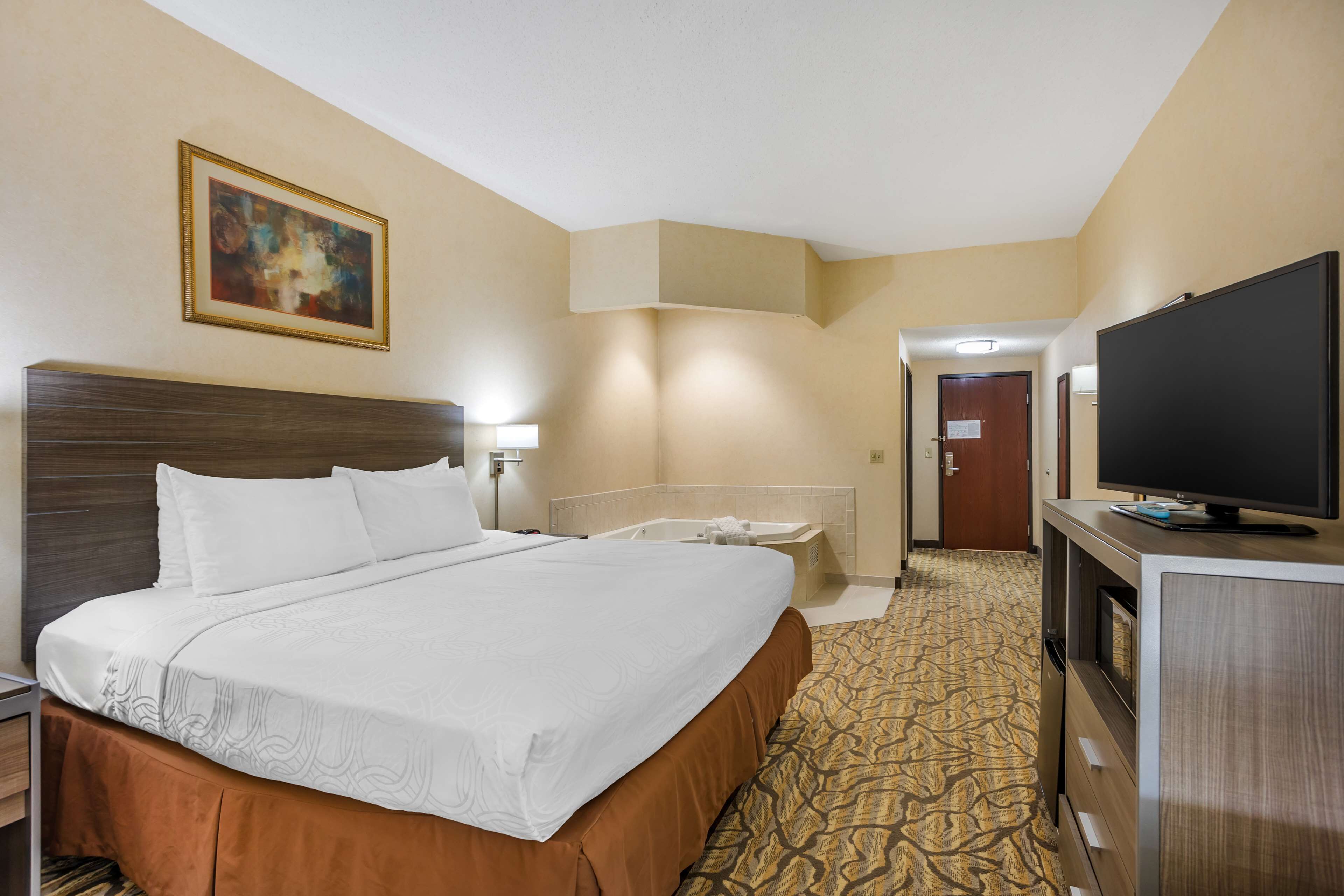 Quarto de hotel com uma cama grande, televisão, banheiro com banheira e um quadro na parede.
