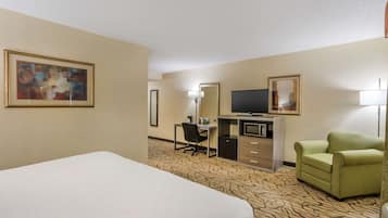 Una habitación de hotel con cama, escritorio con computadora, televisión, sillón verde y piso alfombrado.