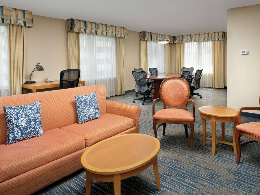 A hotel room with an orange sofa, two blue patterned pillows, a wooden coffee table, and a conference table with four chairs.