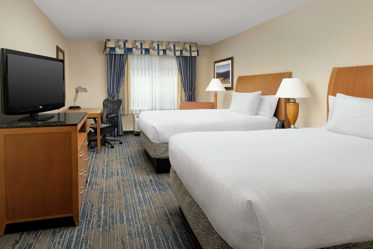 A hotel room with two beds, a desk with a television, a chair, and a carpeted floor.