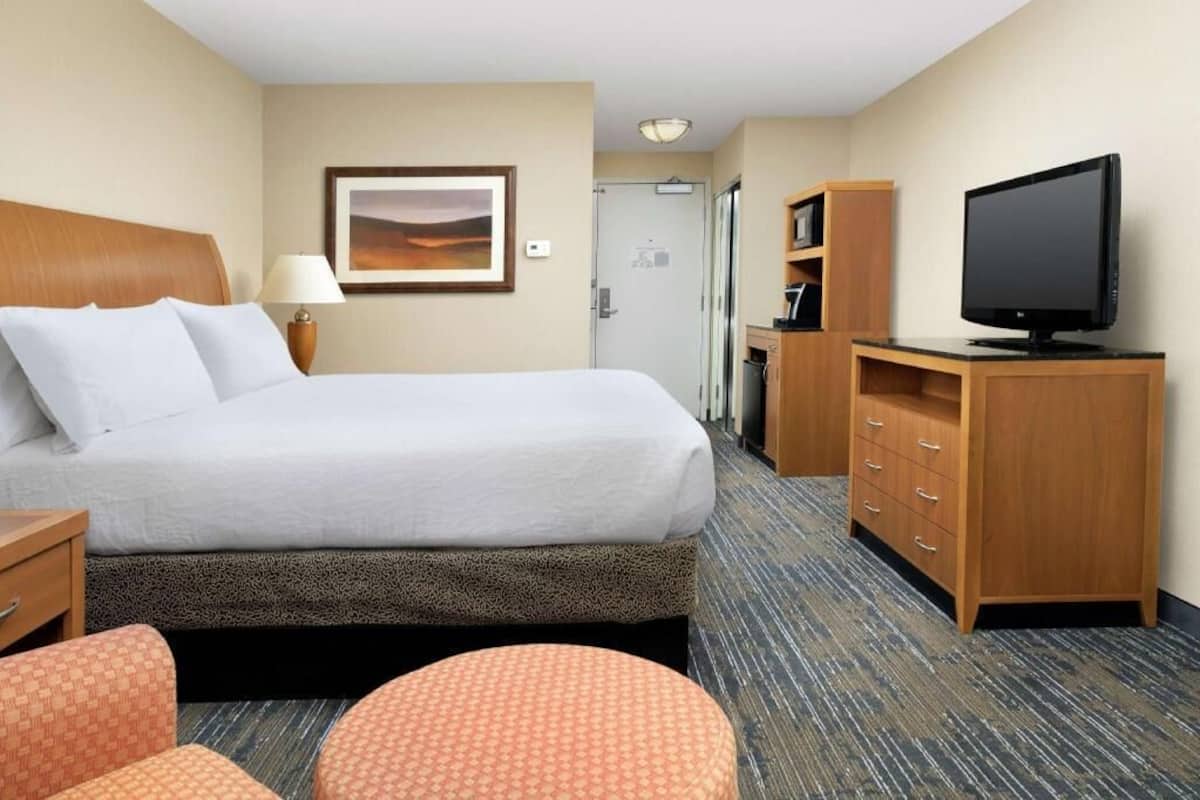 A hotel room with a bed, a television, a desk, a chair, and a small table.