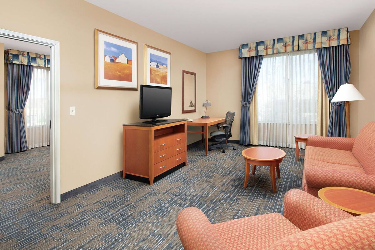 A hotel room with a desk, a television, a sofa, and a chair.