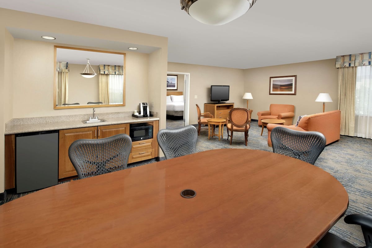 A hotel room with a dining table, chairs, a TV, a sofa, and a small kitchen area.