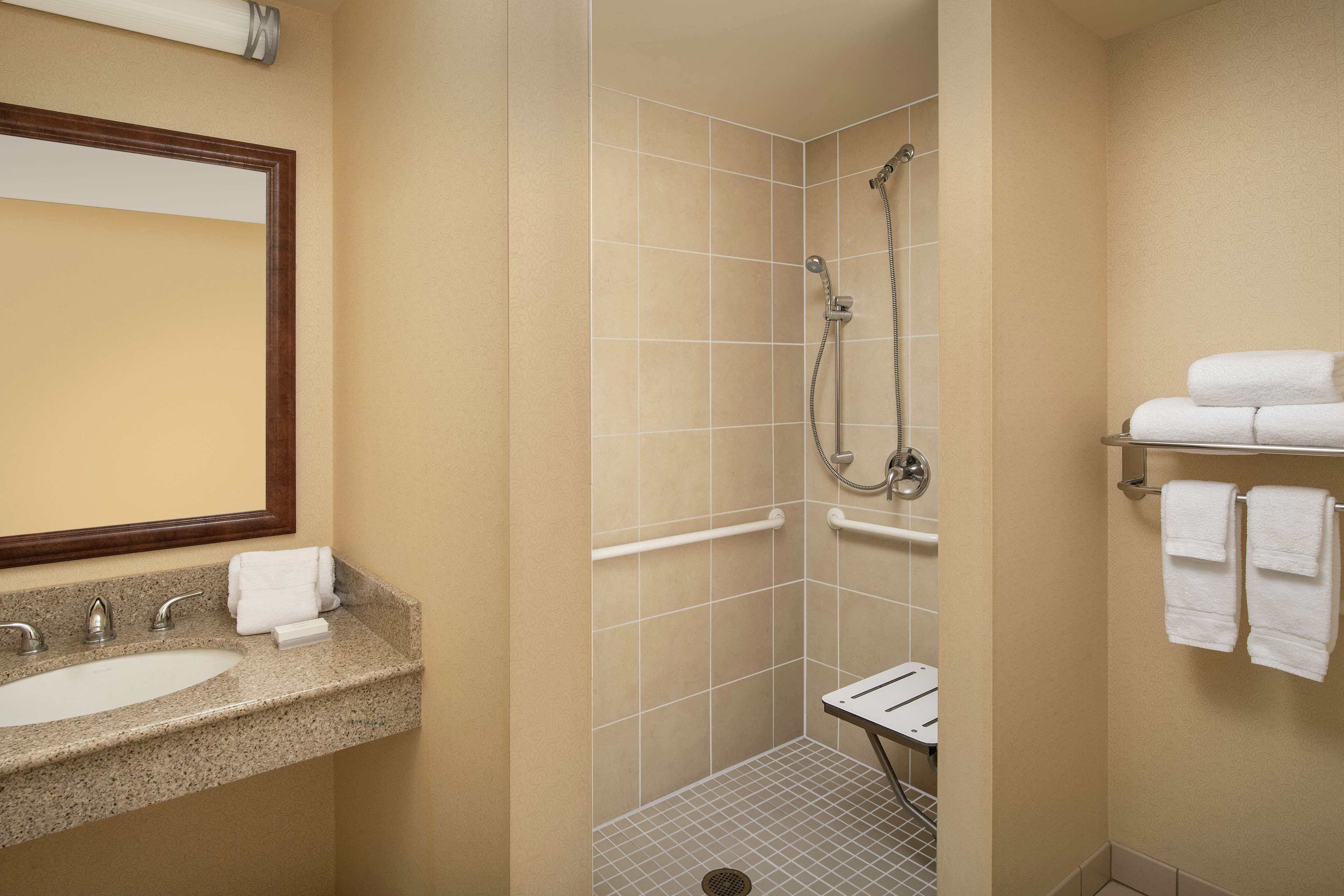 Un baño con lavamanos, espejo, ducha y toallero.
