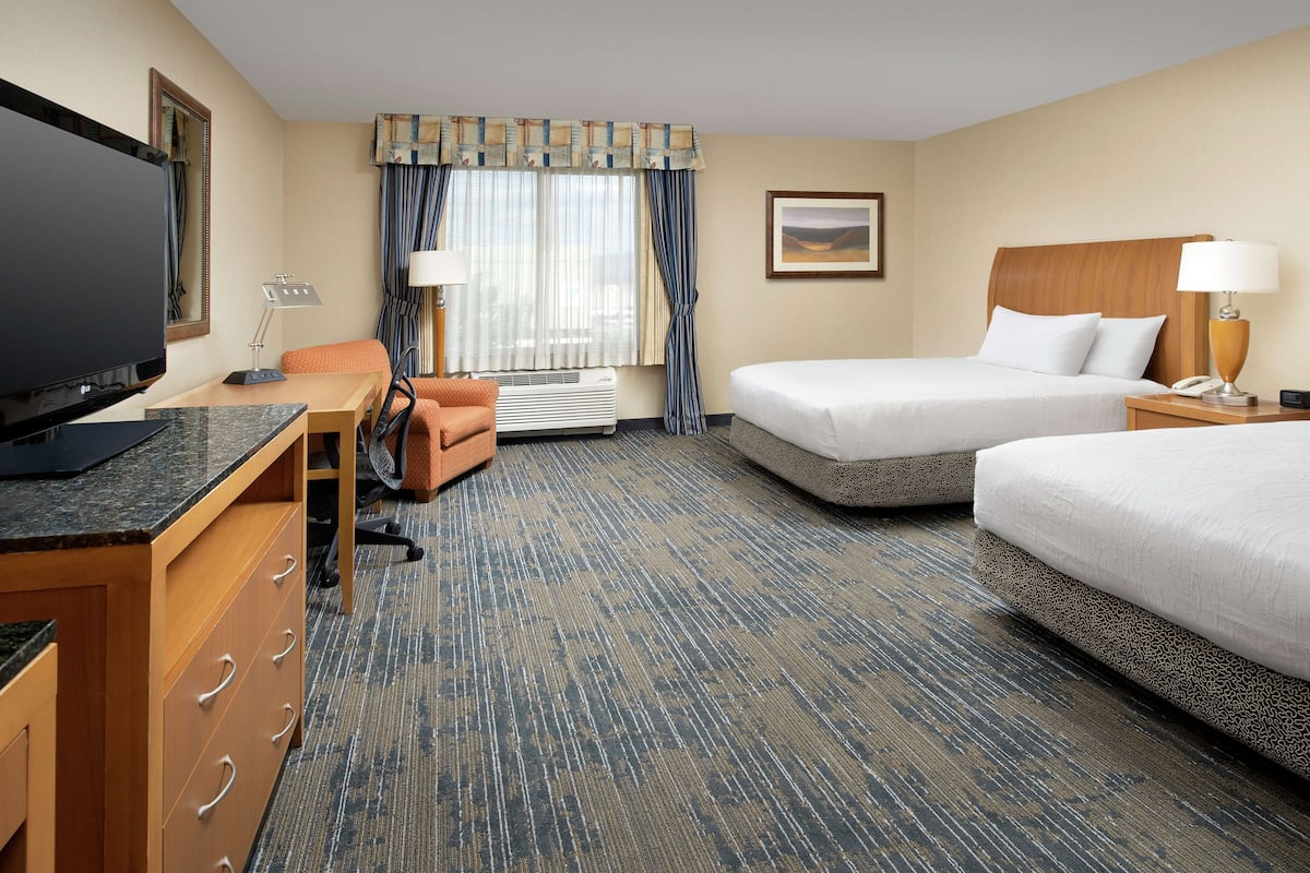 A hotel room with a desk, two beds, a television, and a window with curtains.