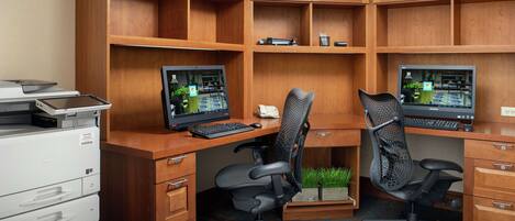 A workspace with two desks, each with a computer and keyboard, surrounded by wooden cabinets and drawers.