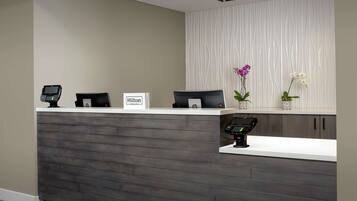 A hotel reception desk with a modern design, featuring a wood-textured counter, a digital payment terminal, and a sign indicating the hotel name.