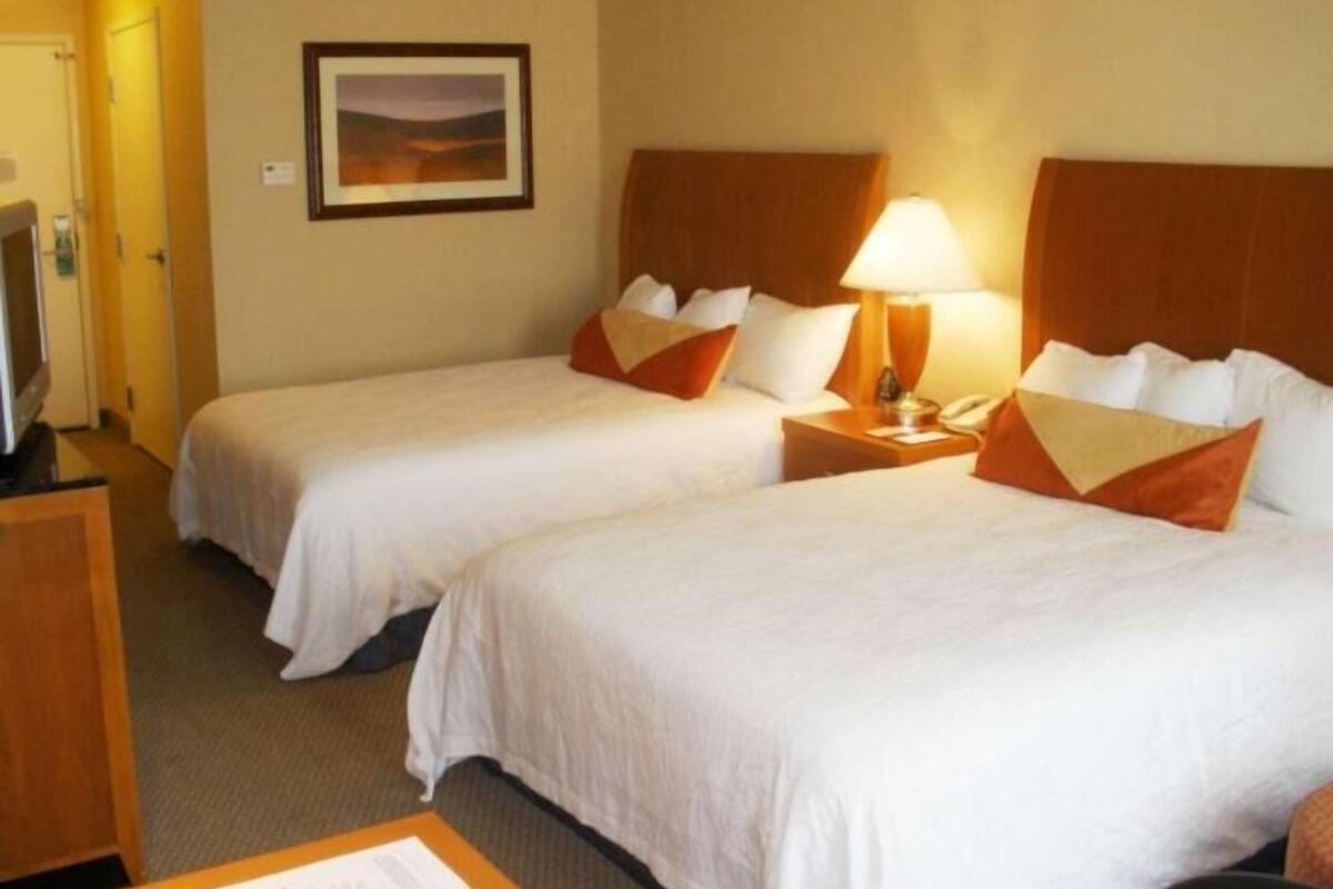 A hotel room with two beds, a television, a framed picture on the wall, and a bedside table with a lamp.