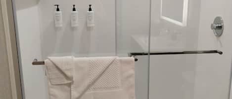 A glass-enclosed shower with a white towel hanging on a metal bar.