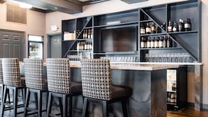 A bar area with a marble countertop, black bar stools, and shelves stocked with bottles and glasses.