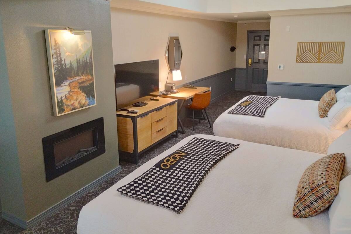 Habitación de hotel con dos camas, un escritorio con lámpara, un cuadro en la pared y una puerta al fondo.