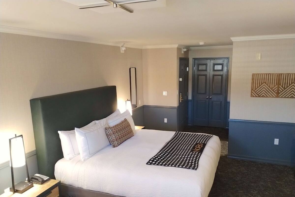 Una habitación de hotel con una cama grande, una mesita de noche con lámpara, teléfono y un espejo en la pared.
