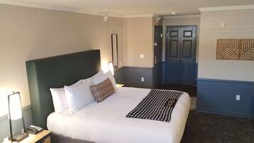A hotel room with a large bed, a bedside table with a lamp, a telephone, and a wall-mounted mirror.