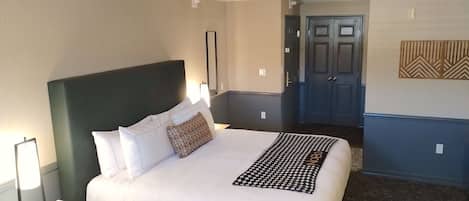 Una habitación de hotel con una cama grande, una mesita de noche con lámpara, teléfono y un espejo en la pared.