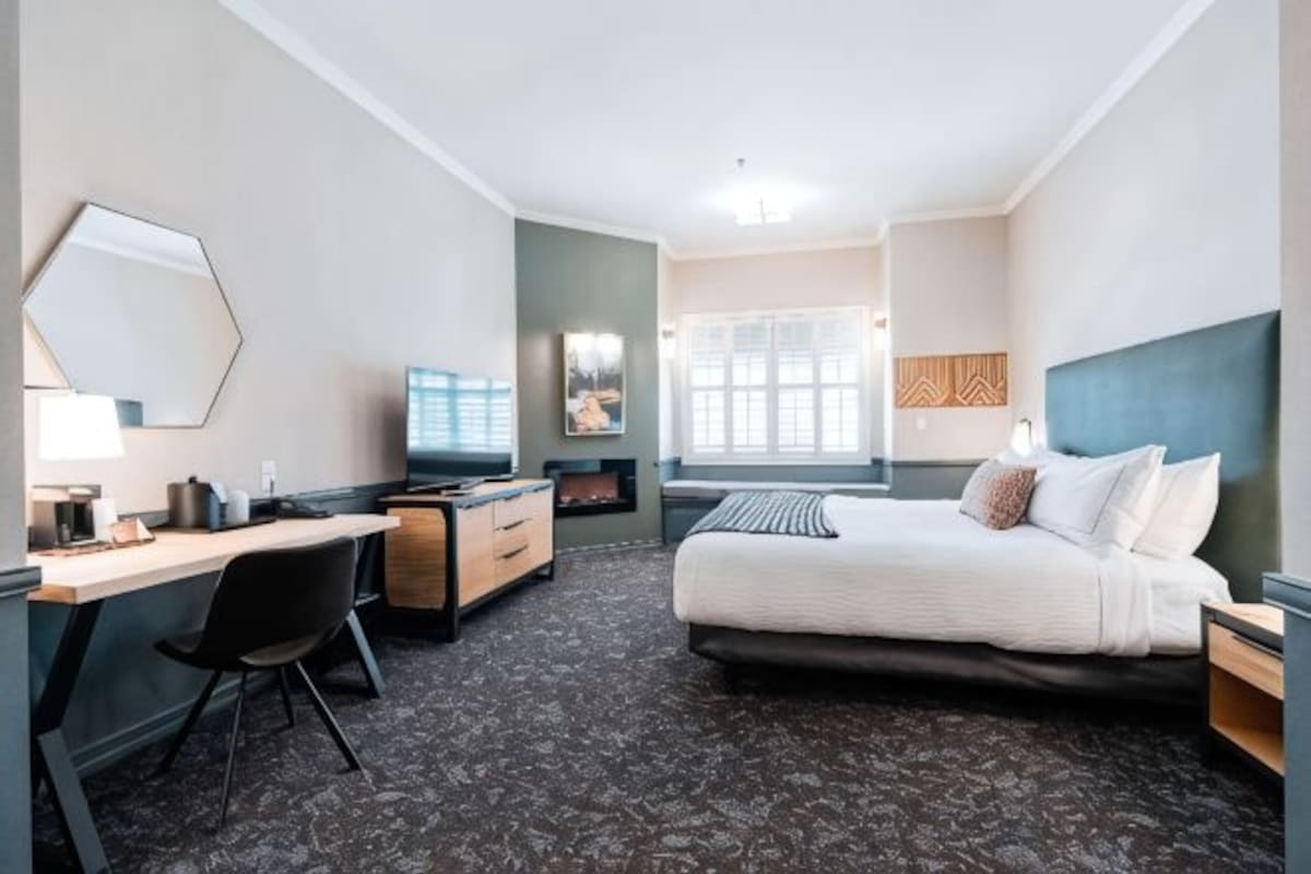 A hotel room with a bed, desk, chair, and a television.