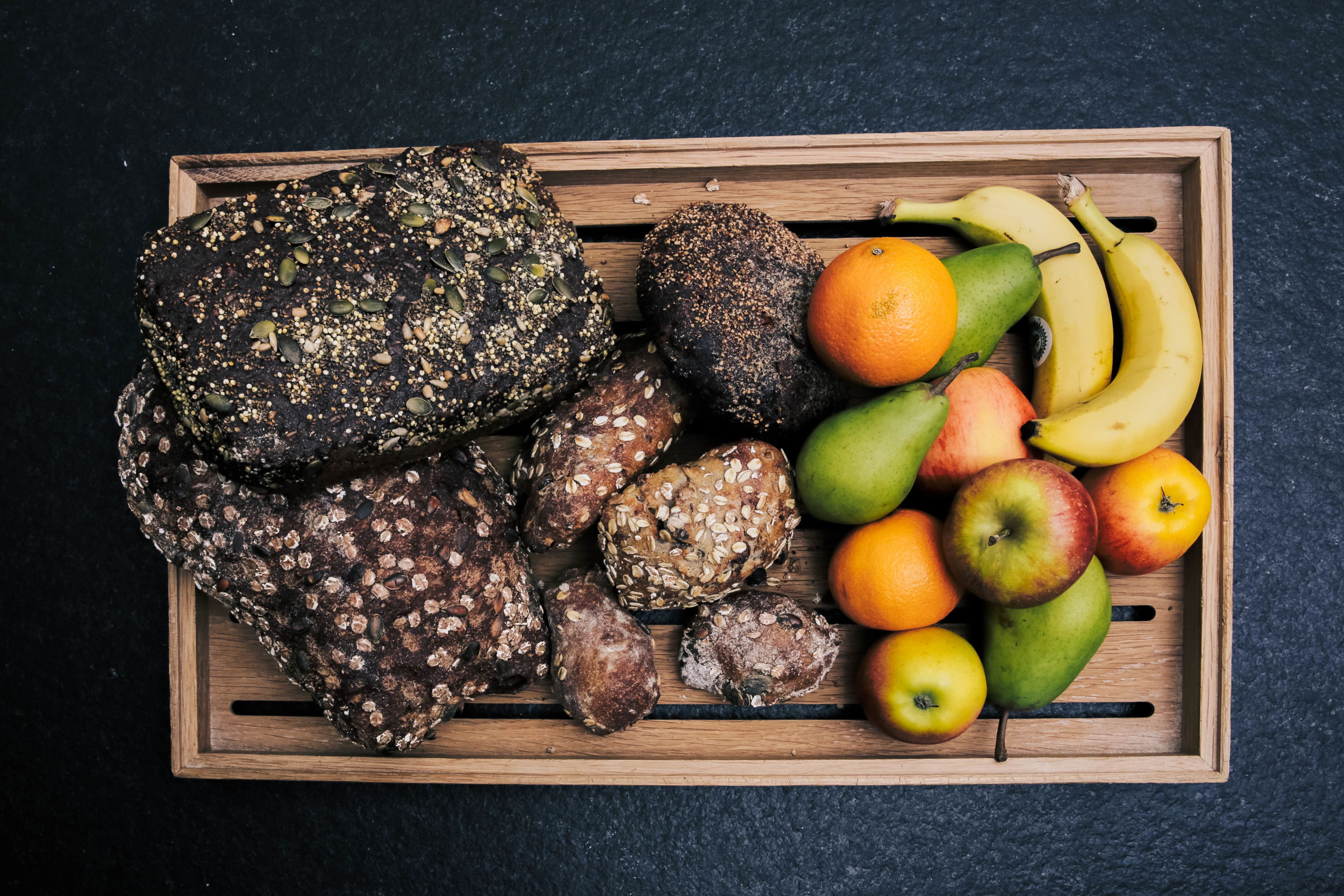 Un plateau en bois contenant divers aliments, notamment du pain, des fruits et des légumes.