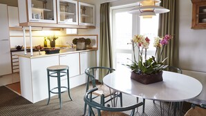 A compact kitchen with a central island, a dining area with a round table and chairs, and a view of the city through a large window.
