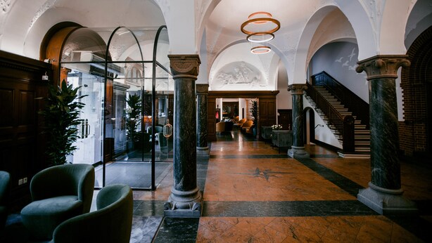 A grand lobby with marble flooring, arched ceilings, and classical columns.