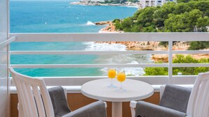 A balcony with two chairs, a table, and two glasses of orange juice. The chairs have towels with "CALA FONT" printed on them. The view includes a beach and ocean. - Cala Font (Salou)