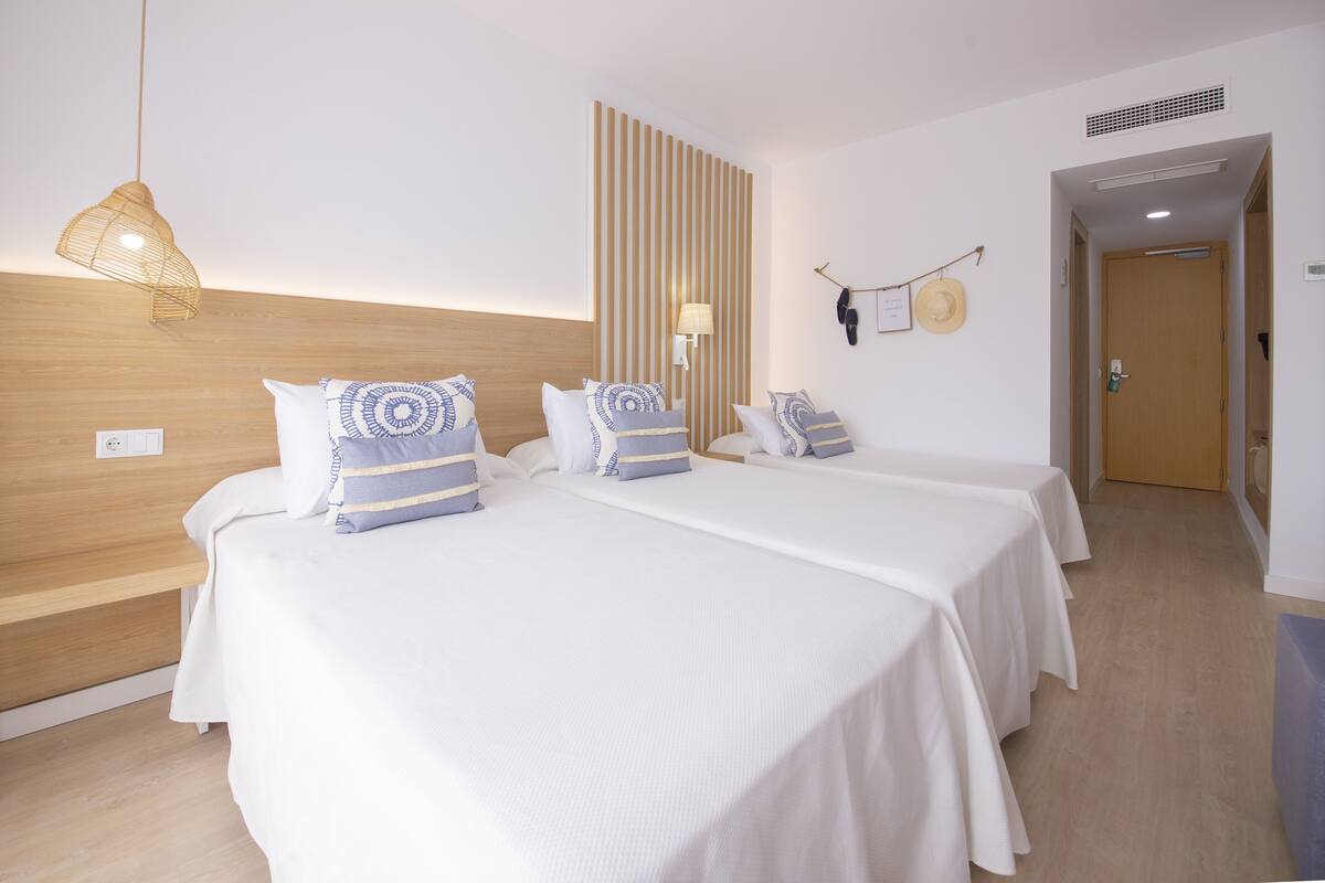 Habitación de hotel con dos camas, cabecera de madera, lámpara de pared y un sombrero en la pared.
