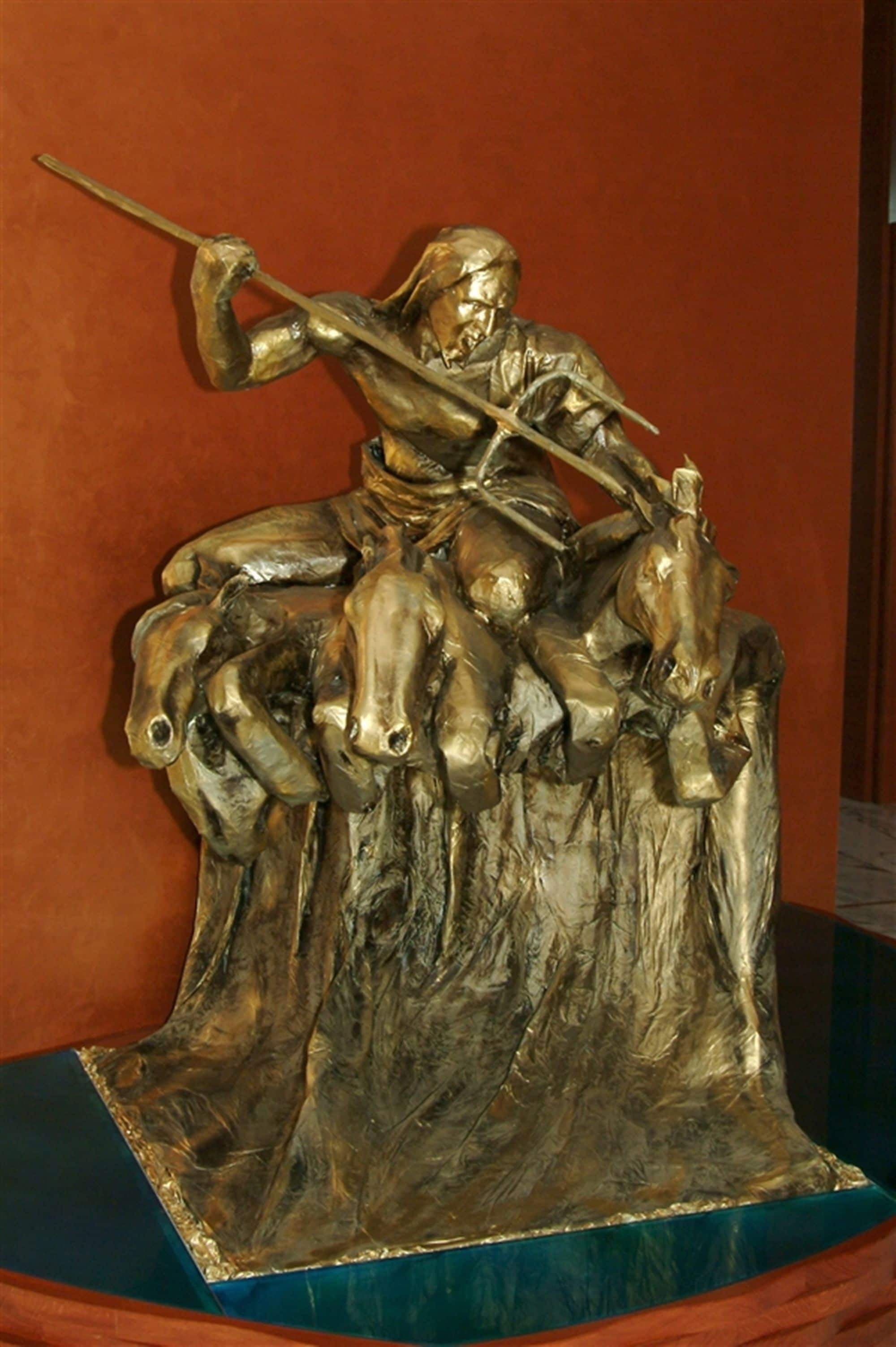 Una estatua de bronce de una figura a caballo, montada sobre una roca con una lanza.