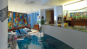 A hotel lobby with a glass floor, colorful abstract art on the walls, a reception desk, and a bar area.