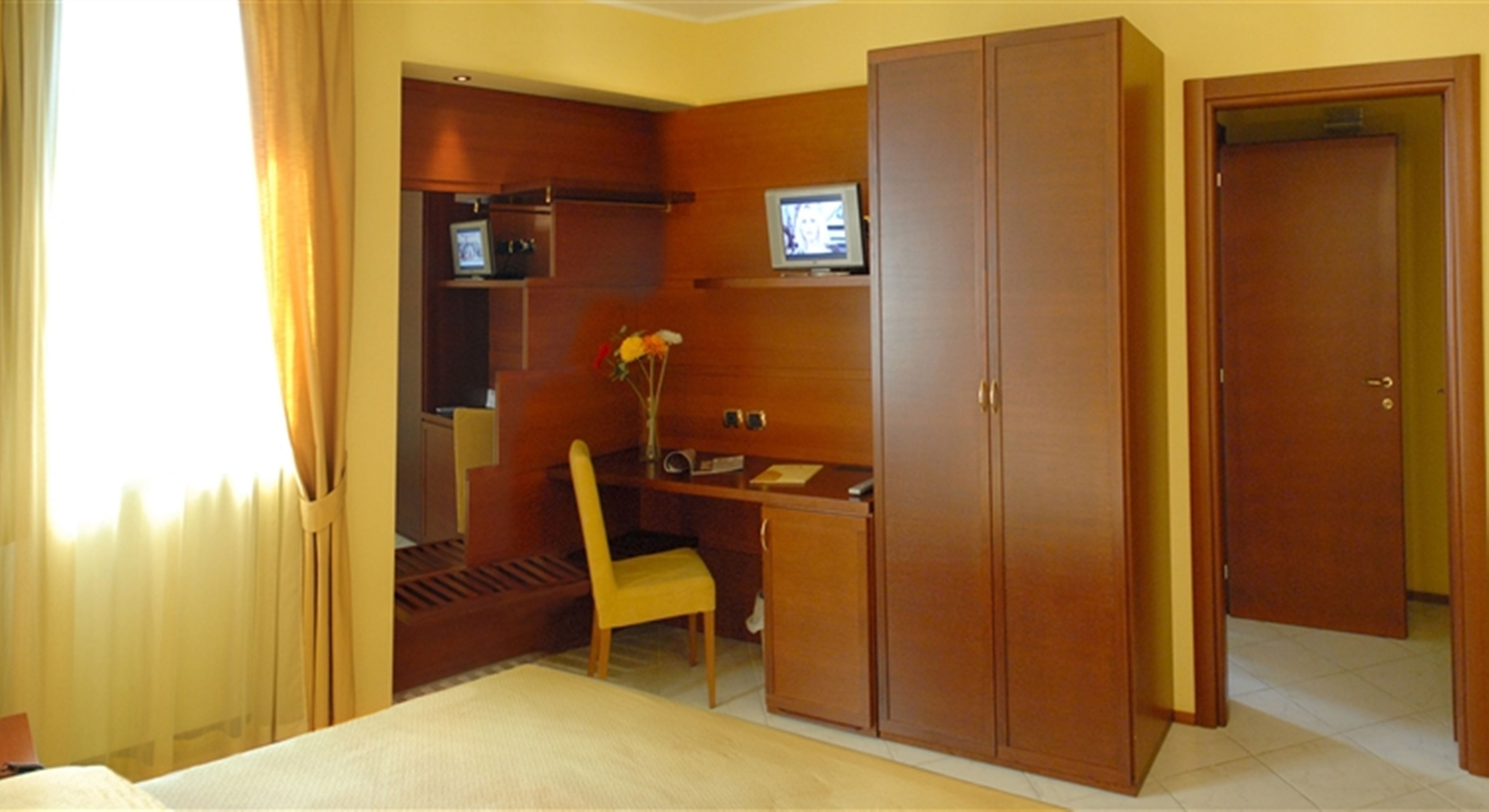 A hotel room with a bed, a desk, a chair, a television, and a wardrobe.