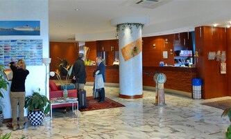 Un vestíbulo con una mesa de recepción, un pilar grande, piso a cuadros y una pared con una foto de un barco.
