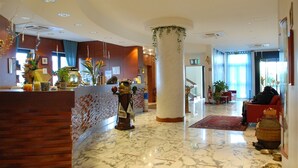 A hotel lobby with a marble floor, a reception desk, a large pillar, and a seating area with a red sofa.