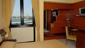 A hotel room with a bed, a desk with a chair, a television, and a view of the sea.