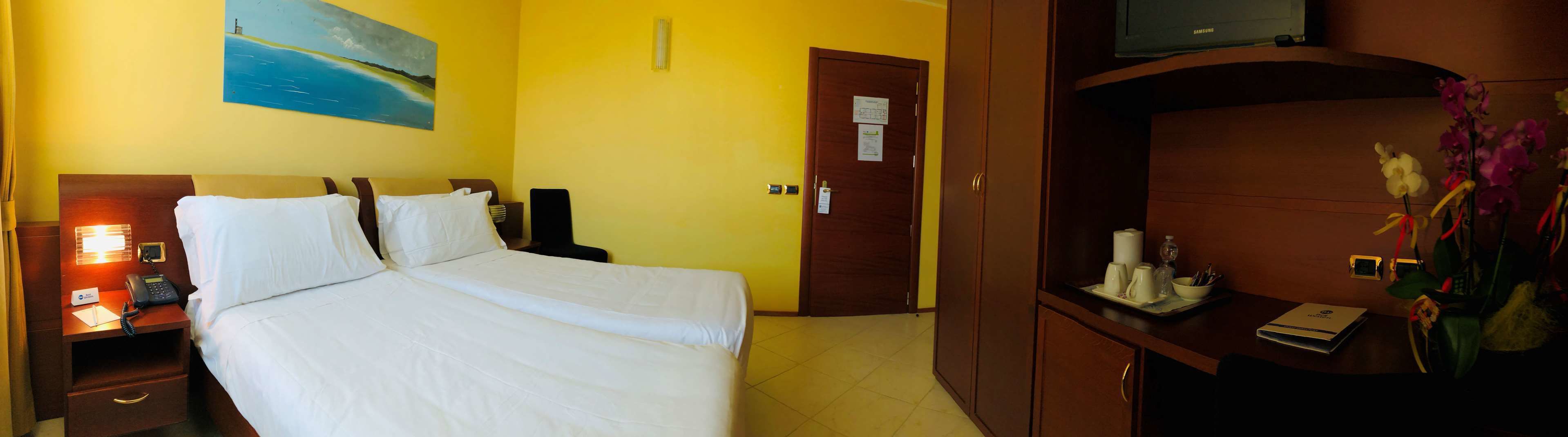 Habitación de hotel con cama, escritorio con teléfono, televisor y un cuadro en la pared.