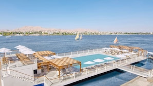 A cruise ship with a pool area, sun loungers, umbrellas, and a view of the Nile River with sailboats. - Iberotel Luxor by JAZ (Luxor)
