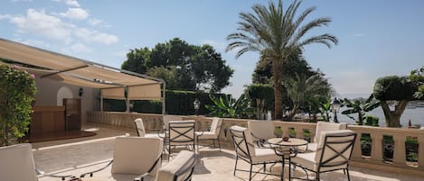 Un patio al aire libre con varias mesas y sillas, una zona de estar cubierta y vistas al mar.