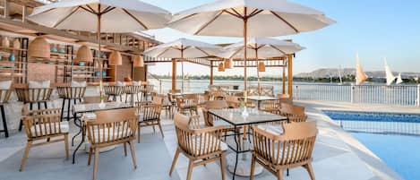A rooftop bar with outdoor seating, umbrellas, and a pool overlooking a scenic view.
