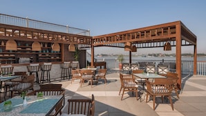 An outdoor patio with wooden furniture and tables, overlooking a body of water. - Iberotel Luxor by JAZ (Luxor)