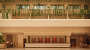A hotel lobby with a high ceiling, multiple floors, and hanging plants. There are several framed artworks on the walls and a reception desk. - Iberotel Luxor by JAZ (Luxor)