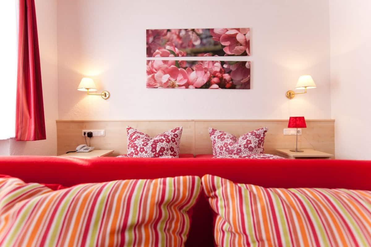 Een hotelkamer met een bed, twee bedlampen, een telefoon, een aan de muur hangend schilderij en een raam met gordijnen.