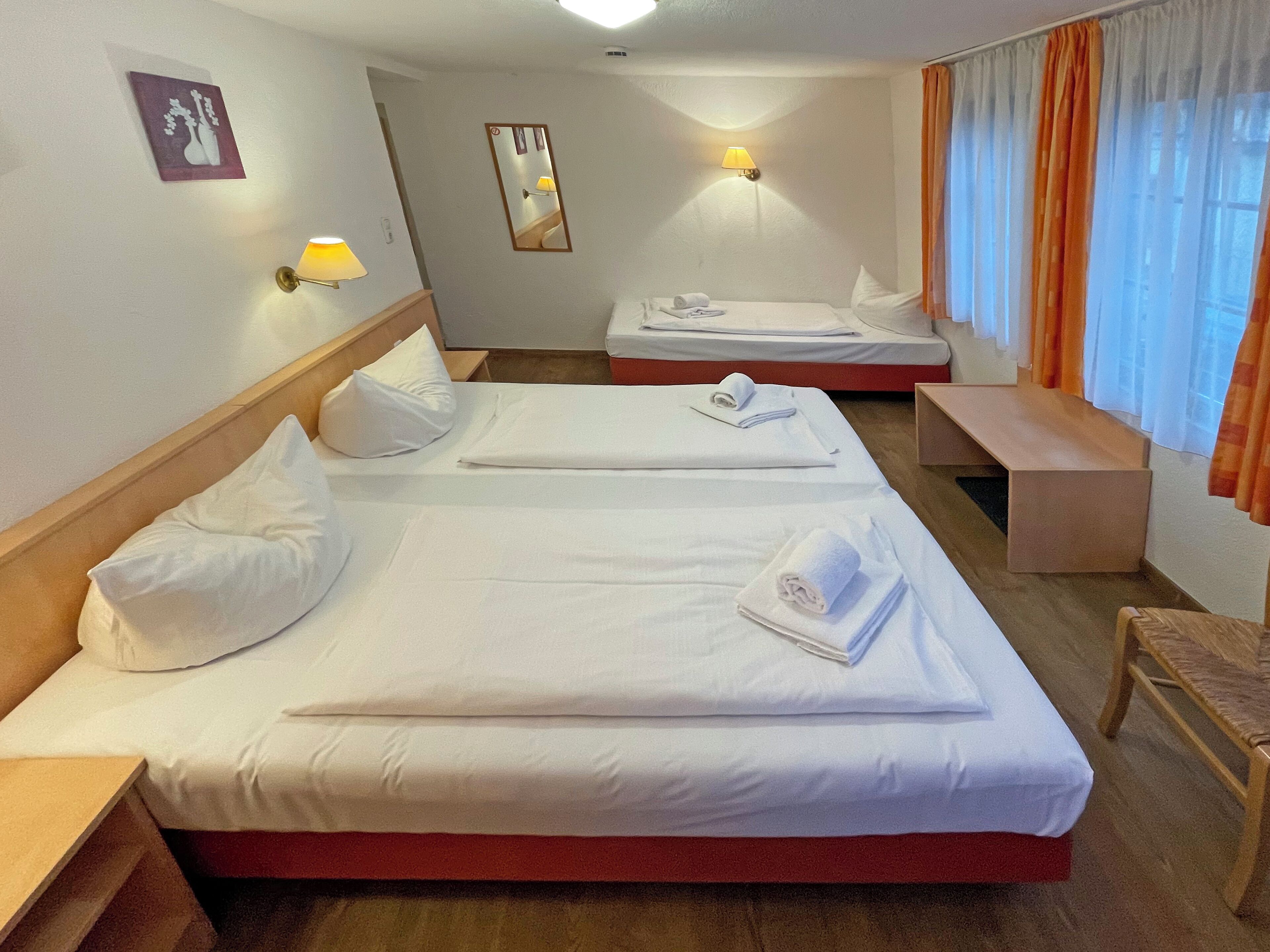 A hotel room with two beds, a bench, a bedside table, a mirror, and a wall-mounted lamp.
