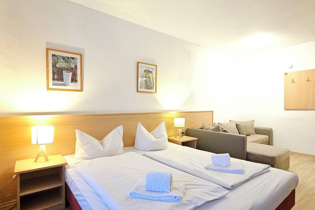 Een hotelkamer met twee bedden, een houten hoofdbord, een bank en twee ingelijste foto’s aan de muur.