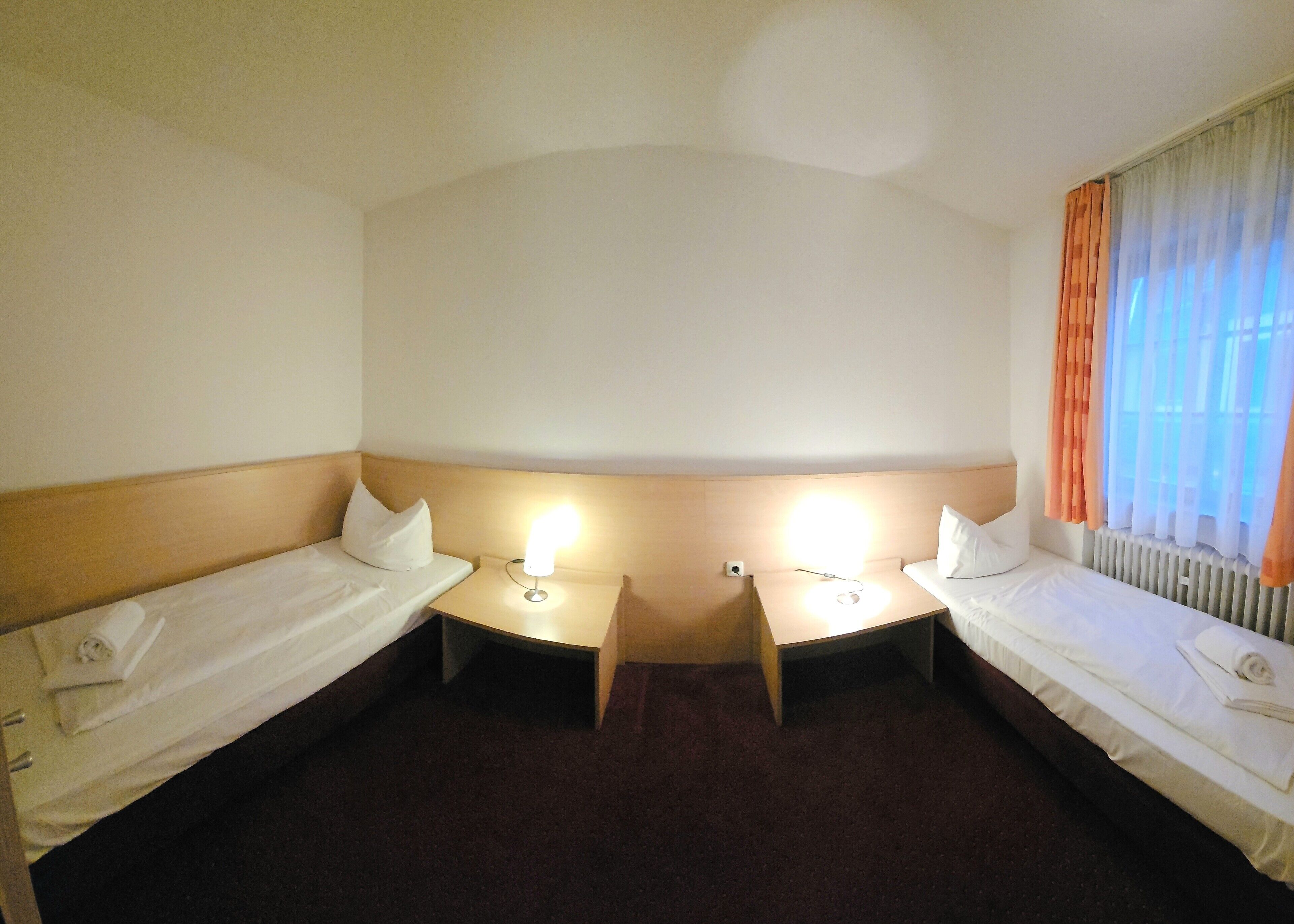 A hotel room with two single beds, a small table, and a nightstand.
