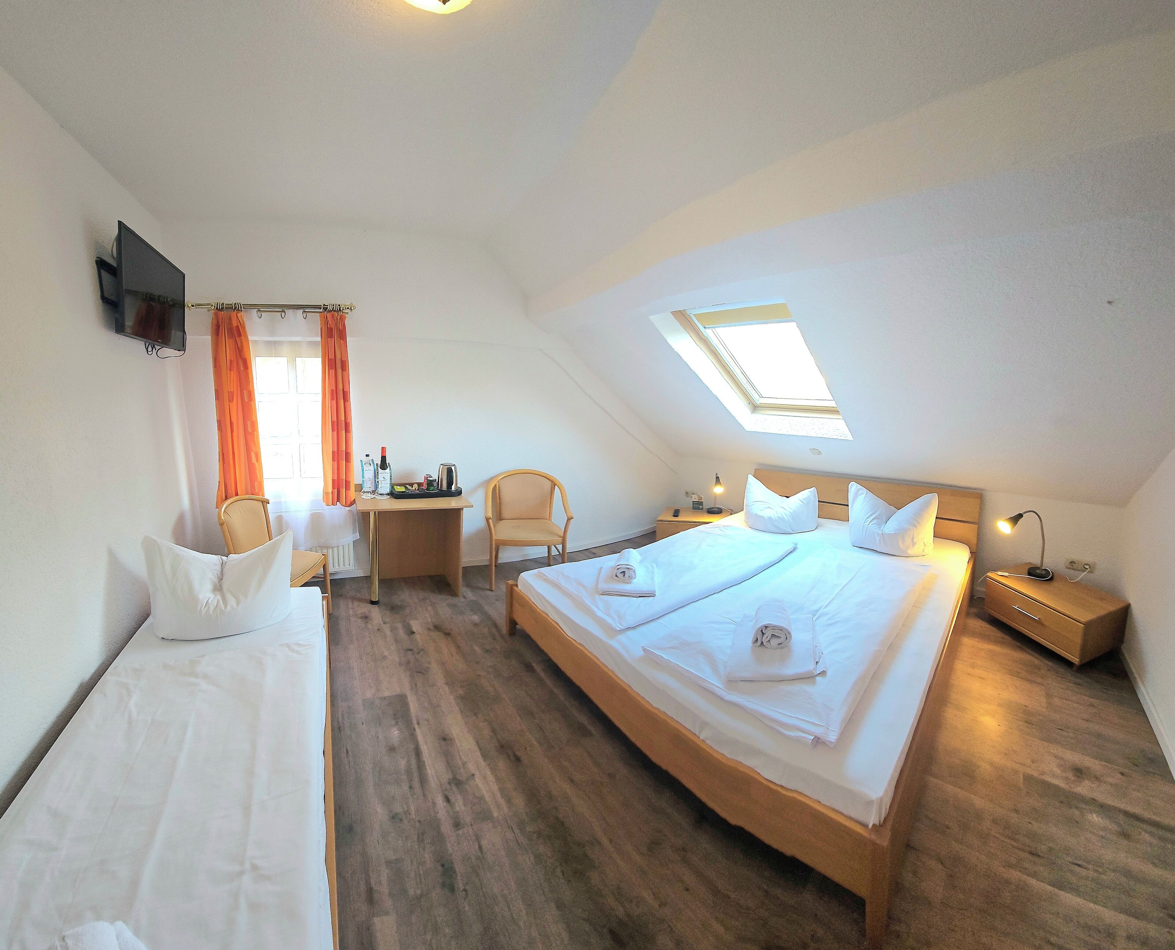 Habitación de hotel con dos camas, un escritorio, una silla, un televisor y un tragaluz.