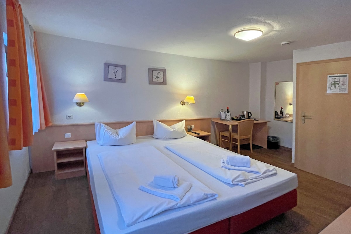 Een hotelkamer met een groot bed, twee nachtkastjes, een bureau, een stoel en een spiegel.