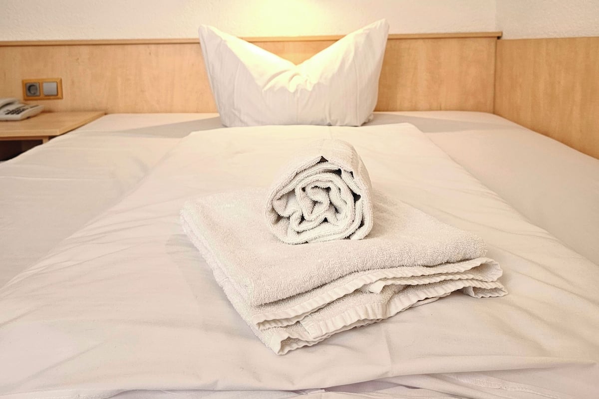 Een hotelkamer met een net opgemaakt bed, een wandlamp en een nachtkastje van hout met een telefoon.