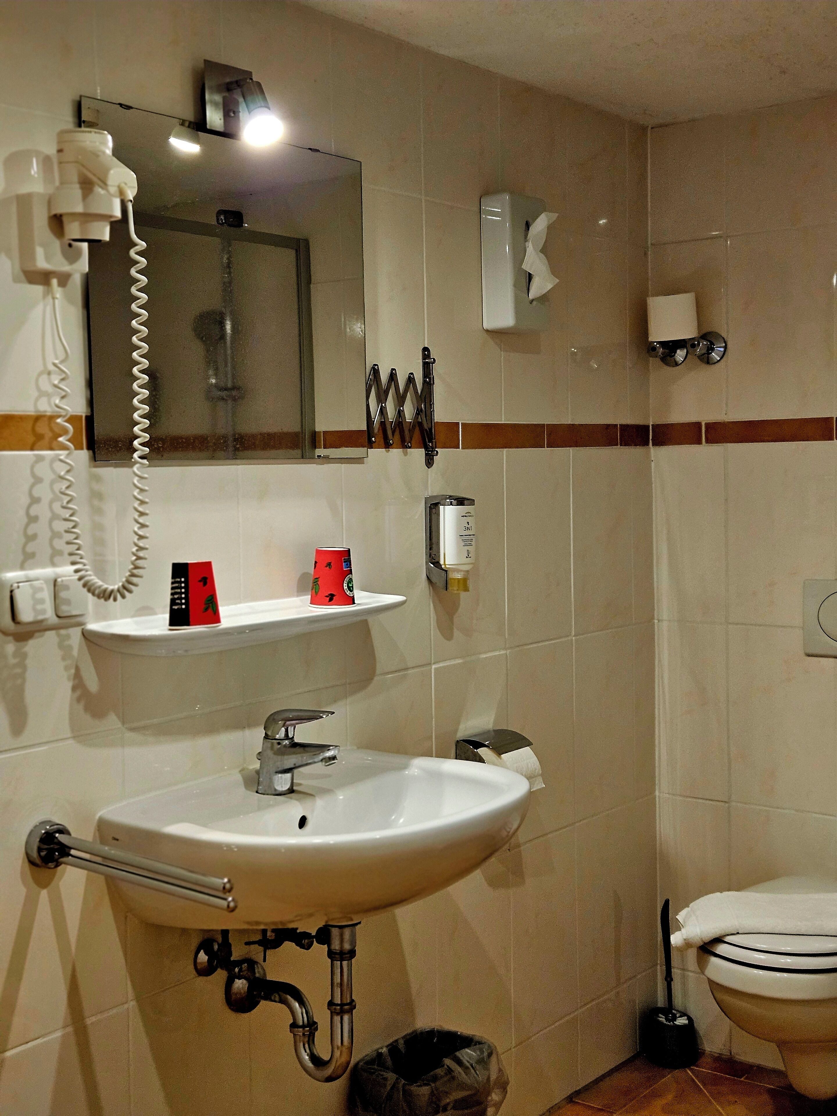 A bathroom with a sink, mirror, towel dispenser, and toilet.