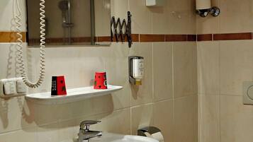 A bathroom with a sink, mirror, towel dispenser, and toilet.