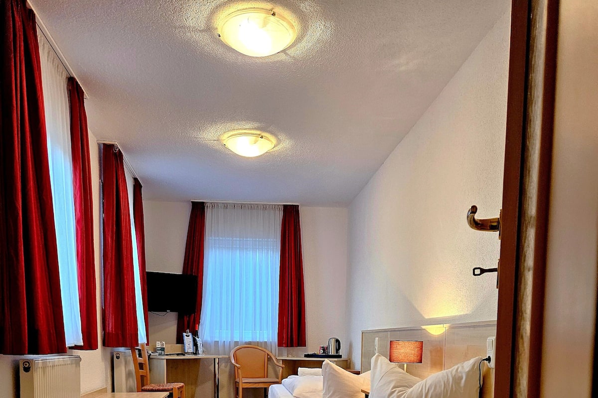 Een hotelkamer met twee bedden, een bureau, een stoel, een radiator en een televisie.