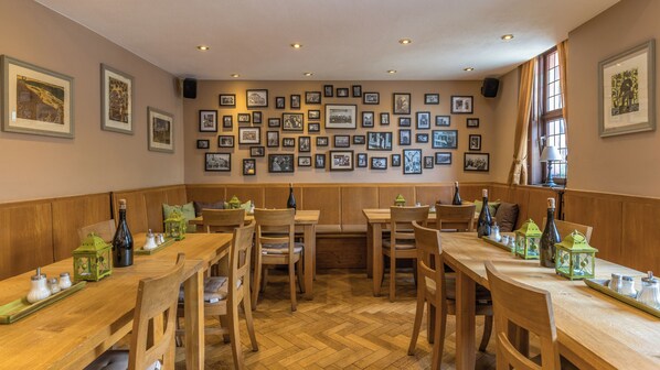 Um restaurante com mesas e bancos de madeira, quadros decorativos nas paredes e um padrão de piso em padrão herringbone.
